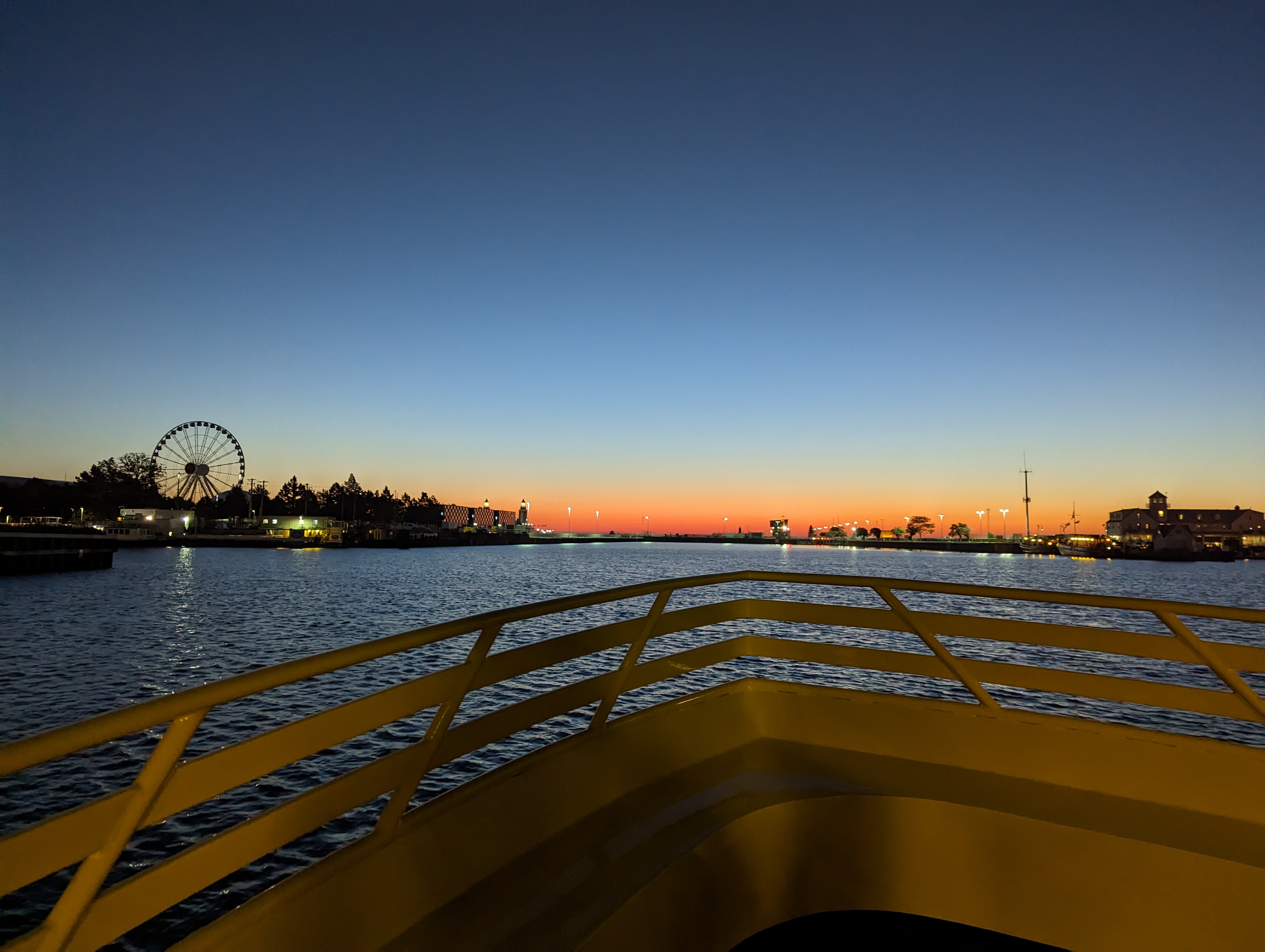 The sunrise over lake Michigan as seen from the Chicago river basin. Off to the left is Navy Pier and its ferris wheel. In the foreground can be seen the front guardrails of a yellow boat, where the shot was taken from.